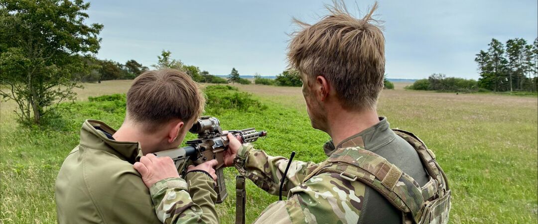 Underviser instruerer elev i at skyde med militært våben udendørs