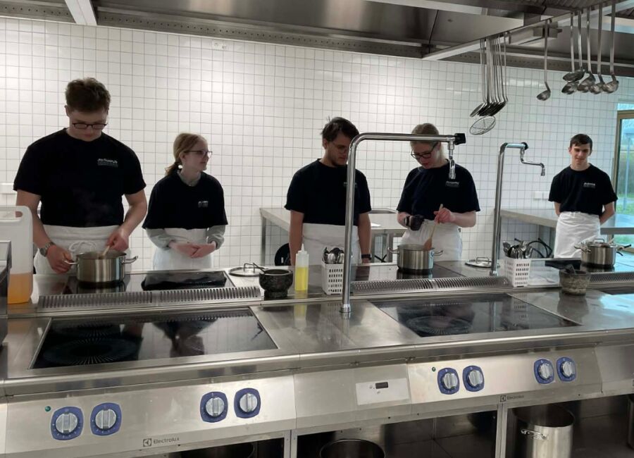 Elever står ved komfur og laver mad i et undervisningskøkken.