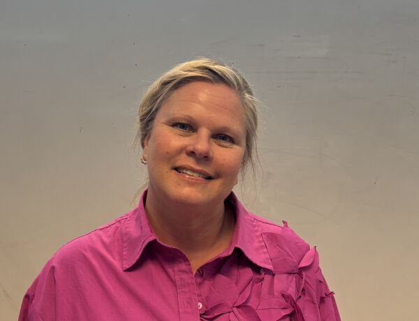 Kvindelig faglærer fra FGU i pink skjorte, smilende mod kamera foran neutral baggrund