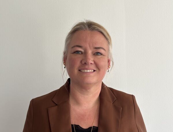 Kvinde i brun blazer smiler mod kamera foran lys baggrund