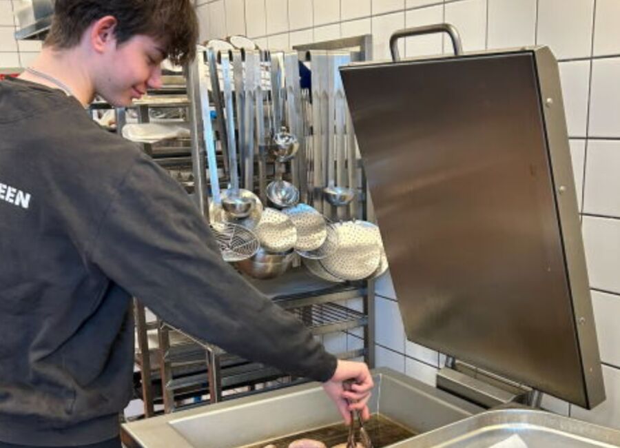 Ung person tilbereder pølser i et storkøkken.