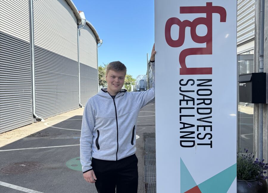 Tobias Bastholm står ved skiltet foran FGU Nordvestsjælland i Holbæk.