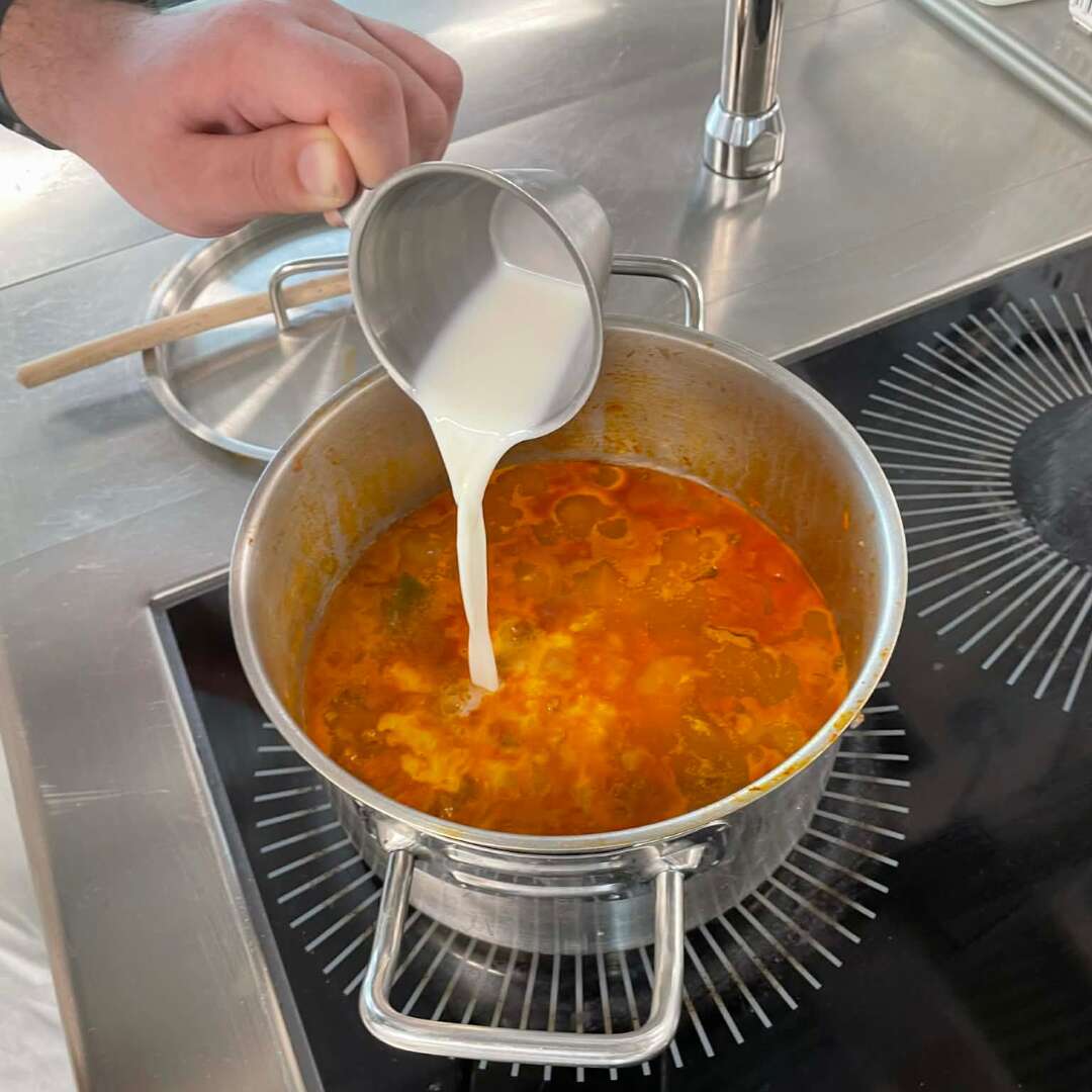 Fløde hældes i en gryde med suppe på komfuret.