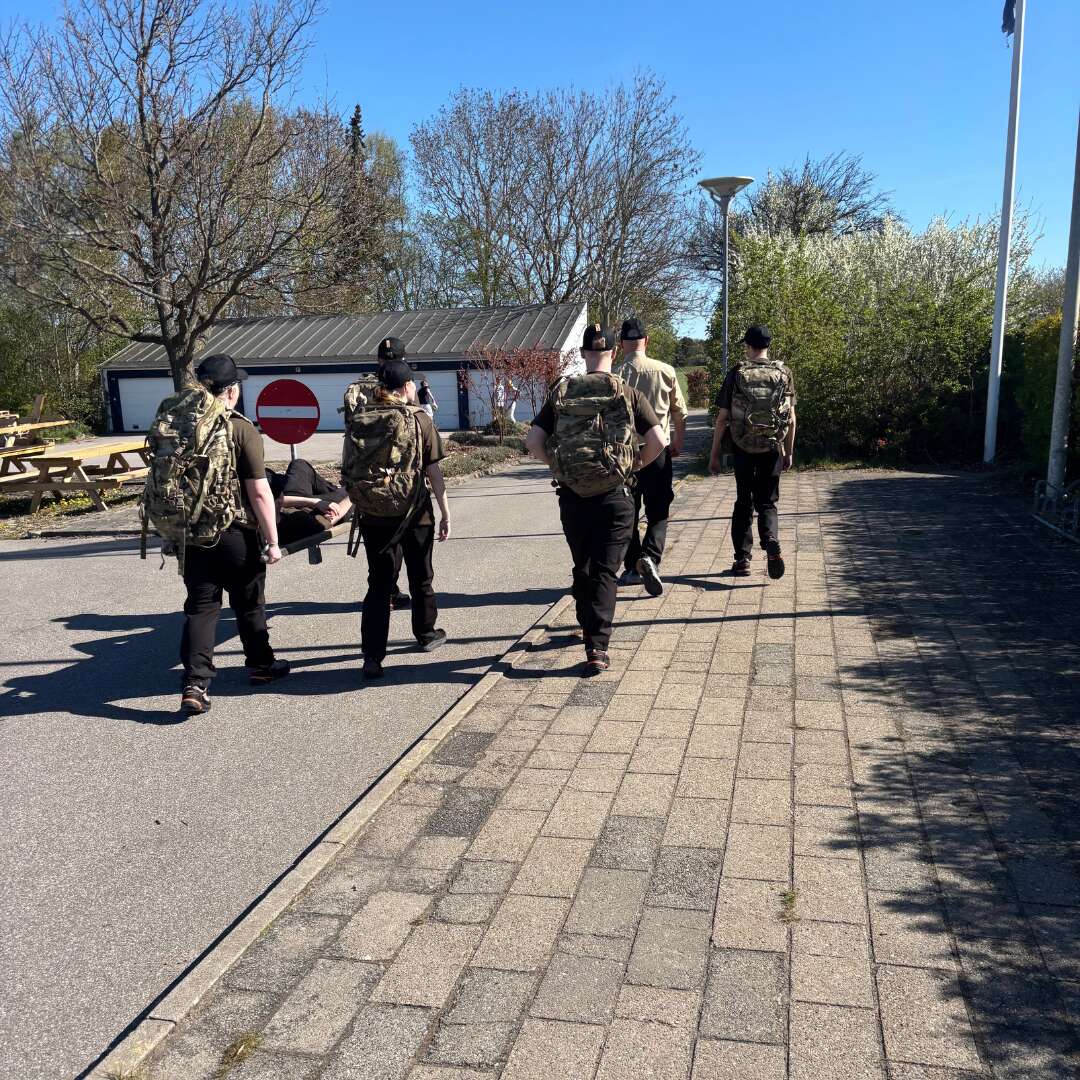 Elever går med oppakning og bærer en person på båre