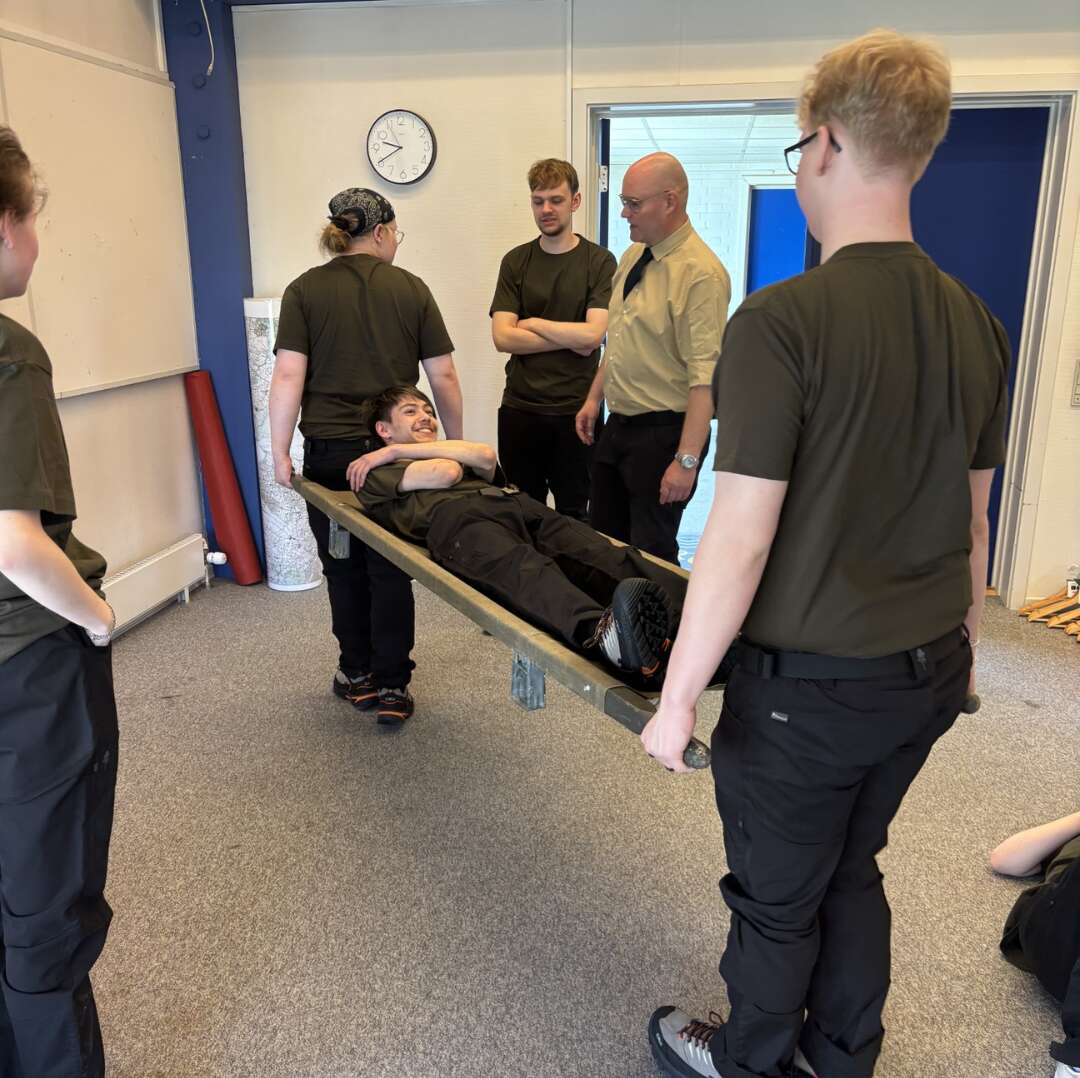 Elever øver båretransport indendørs, mens underviser observerer og vejleder