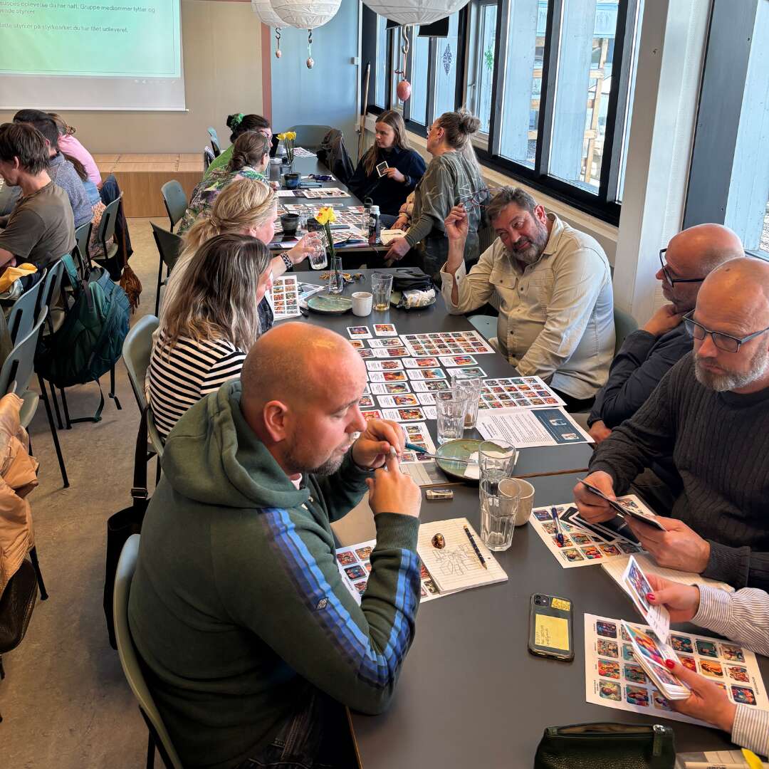 Deltagere omkring et bord bruger billedkort og noter under en fælles aktivitet.