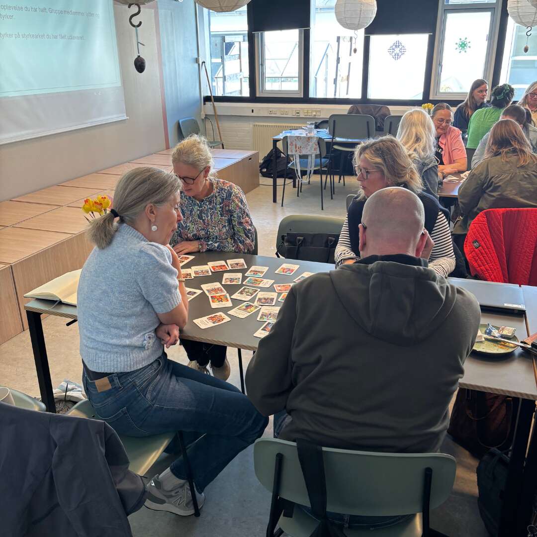 Gruppe af deltagere omkring et bord arbejder med kort som del af en øvelse.