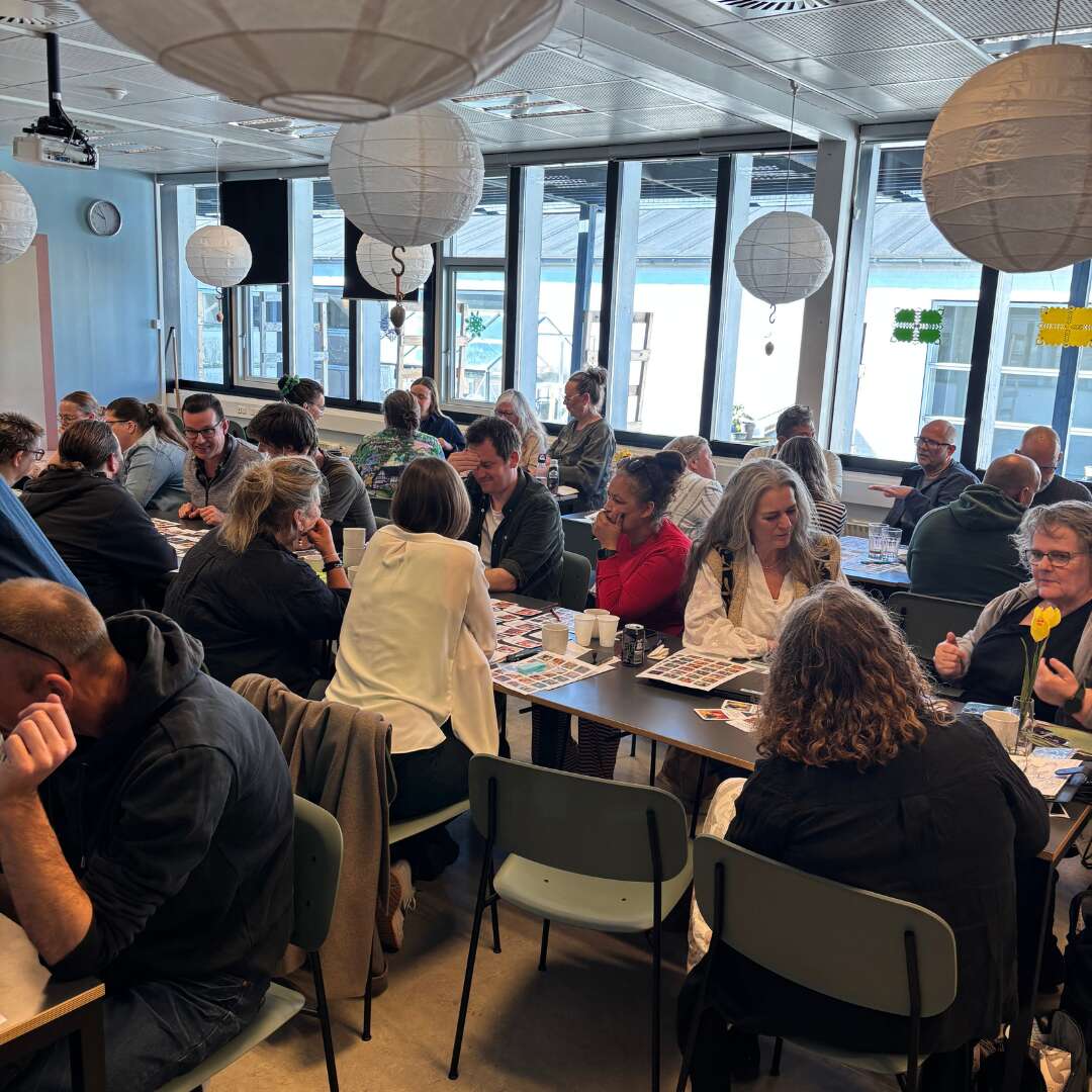 Flere grupper deltager i gruppearbejde ved borde i et lyst kursuslokale.